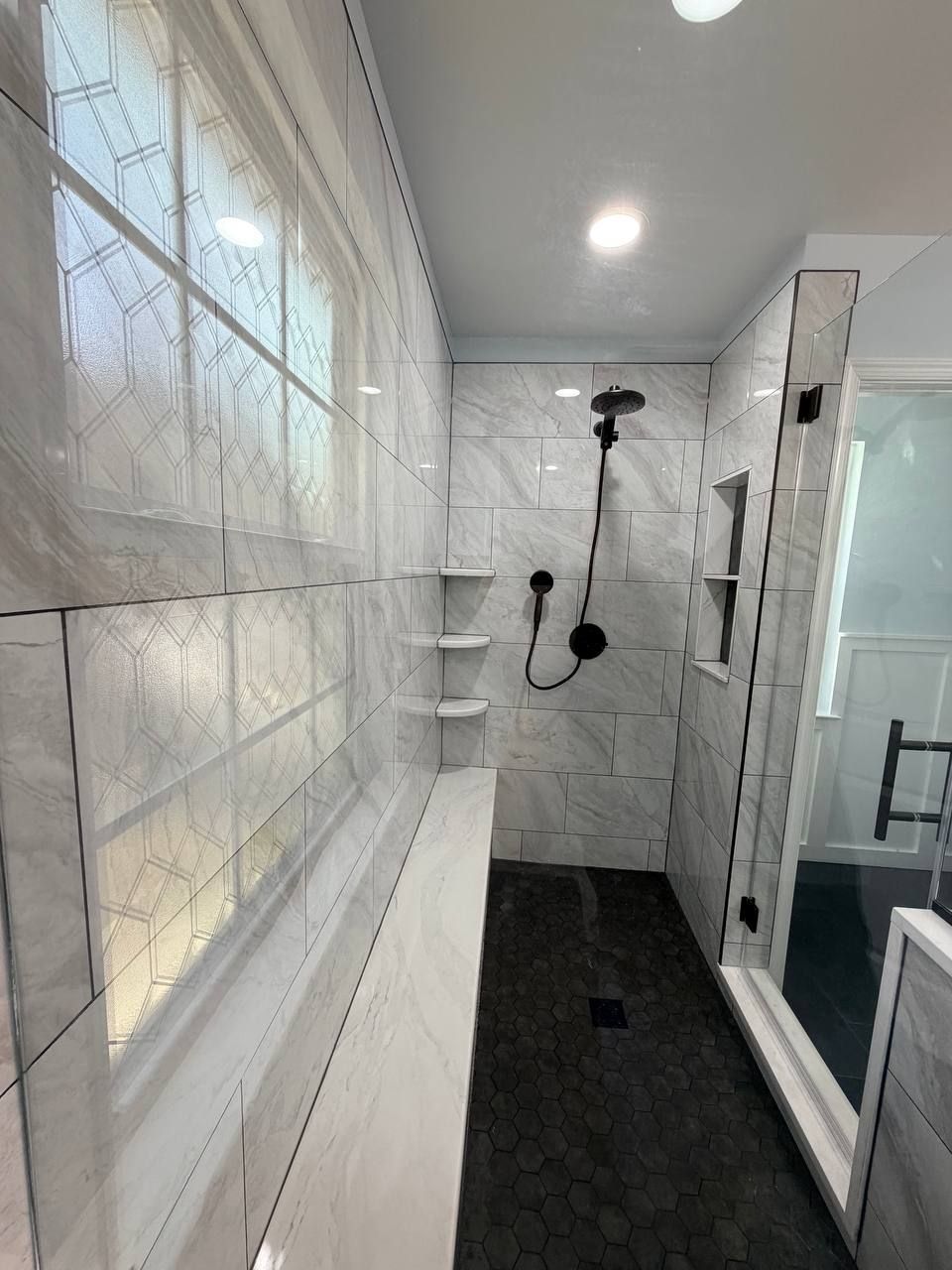 Luxury bathroom remodeling and renovation in Clarksville MD — walk-in shower with white marble tile walls, built-in bench, recessed niche, and black hex floor tile by Handyman on Demand