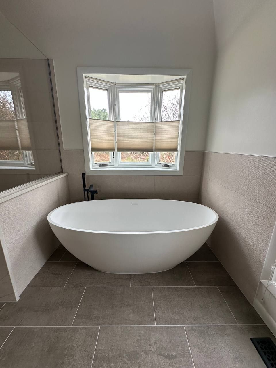 Affordable master bath renovation in Clarksville MD featuring freestanding soaking tub centered under bay window with large format neutral floor tile by local contractor Handyman on Demand