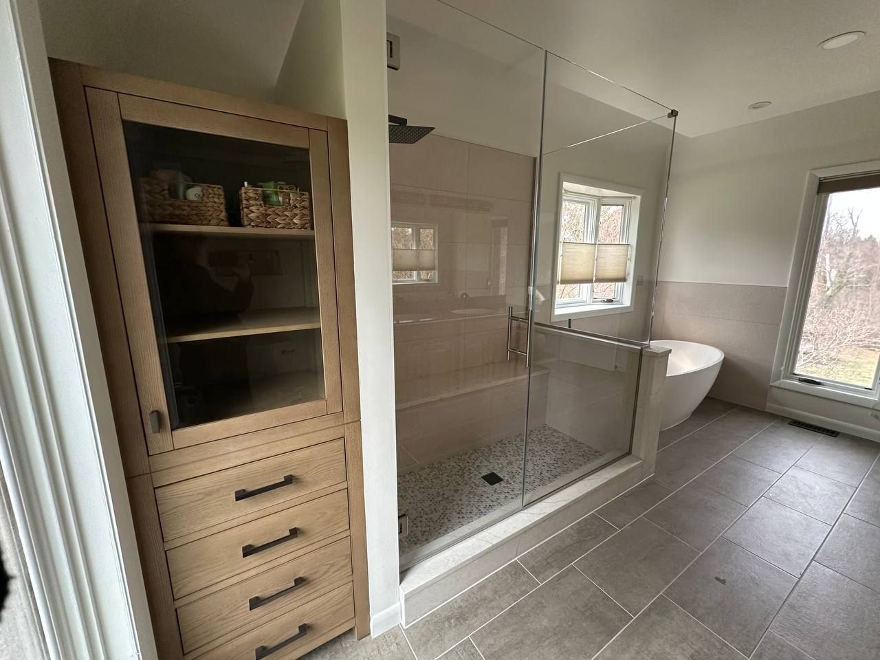 Professional master bathroom renovation in Clarksville Maryland with custom glass shower enclosure, storage tower cabinet, and freestanding soaking tub by Handyman on Demand