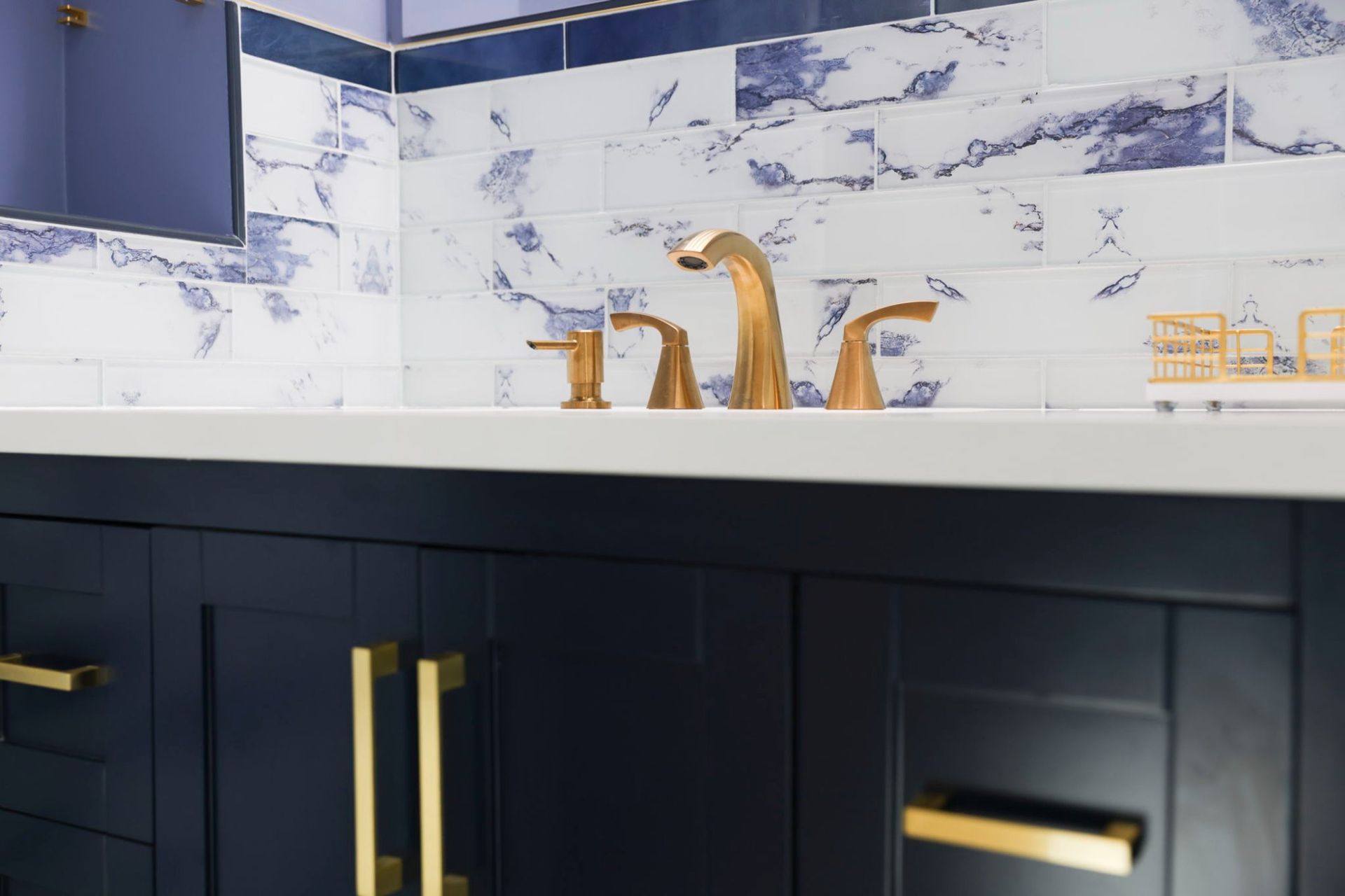 Updated bathroom with a navy vanity, gold faucet and blue marble backsplash by Handyman on Demand