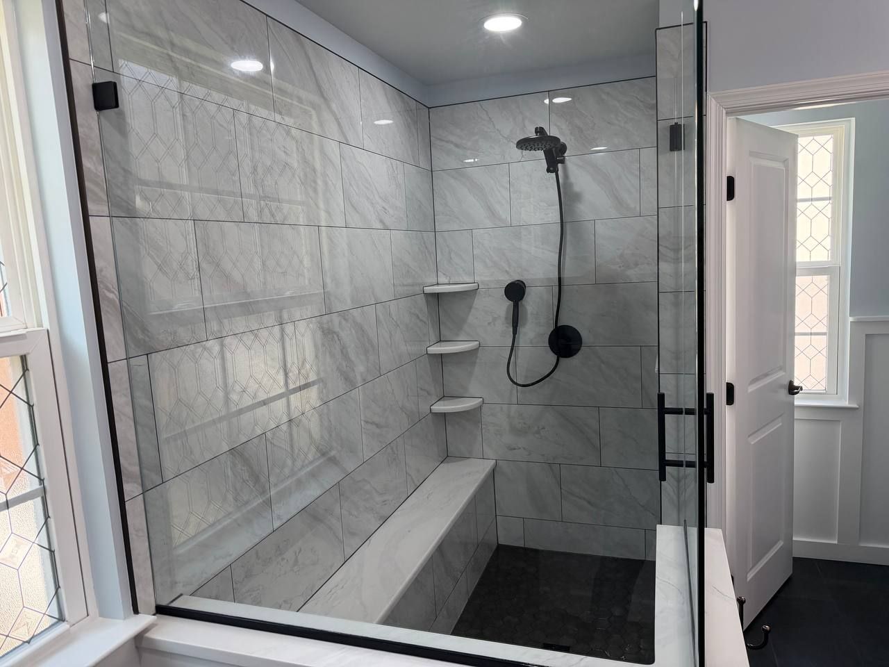 Custom shower remodel and bathroom renovation in Clarksville MD with white marble tile, built-in bench, triple corner shelves, and matte black fixtures by Handyman on Demand