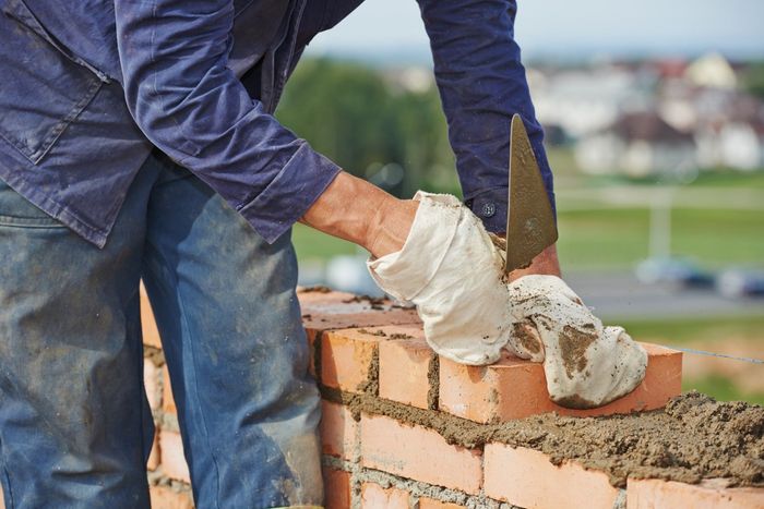 Person wearing gloves using a trowel to spread mortar and lay brick.