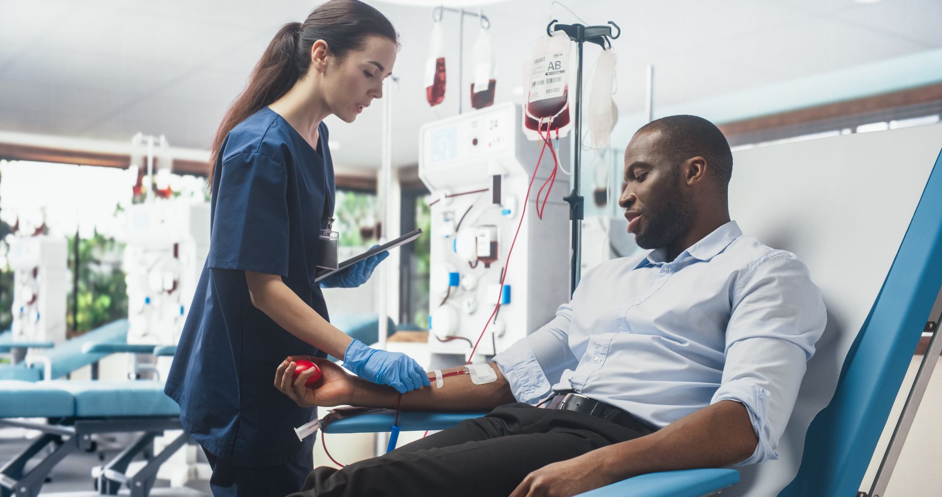 A healthcare professional monitors a person donating blood in a medical facility. A healthcare professional monitors a person donating blood in a medical facility.