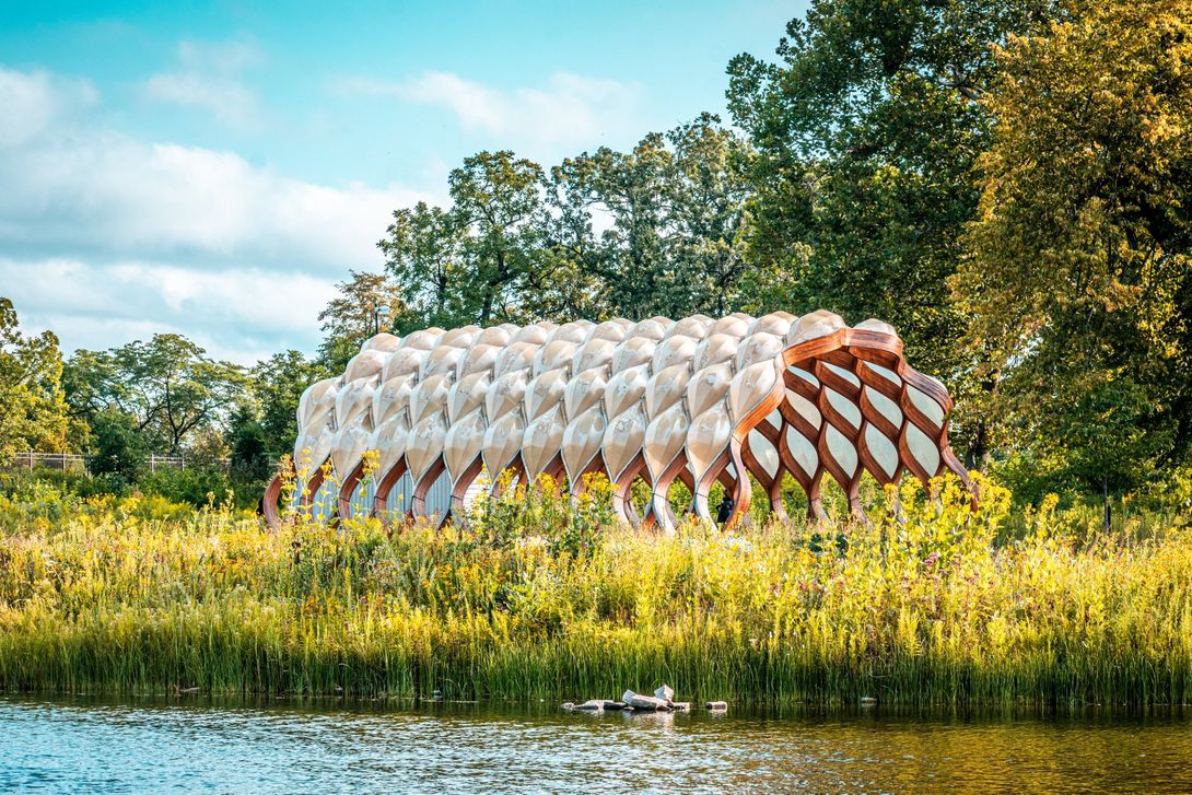 A large building is sitting on top of a grassy hill next to a body of water at Lincoln Park.