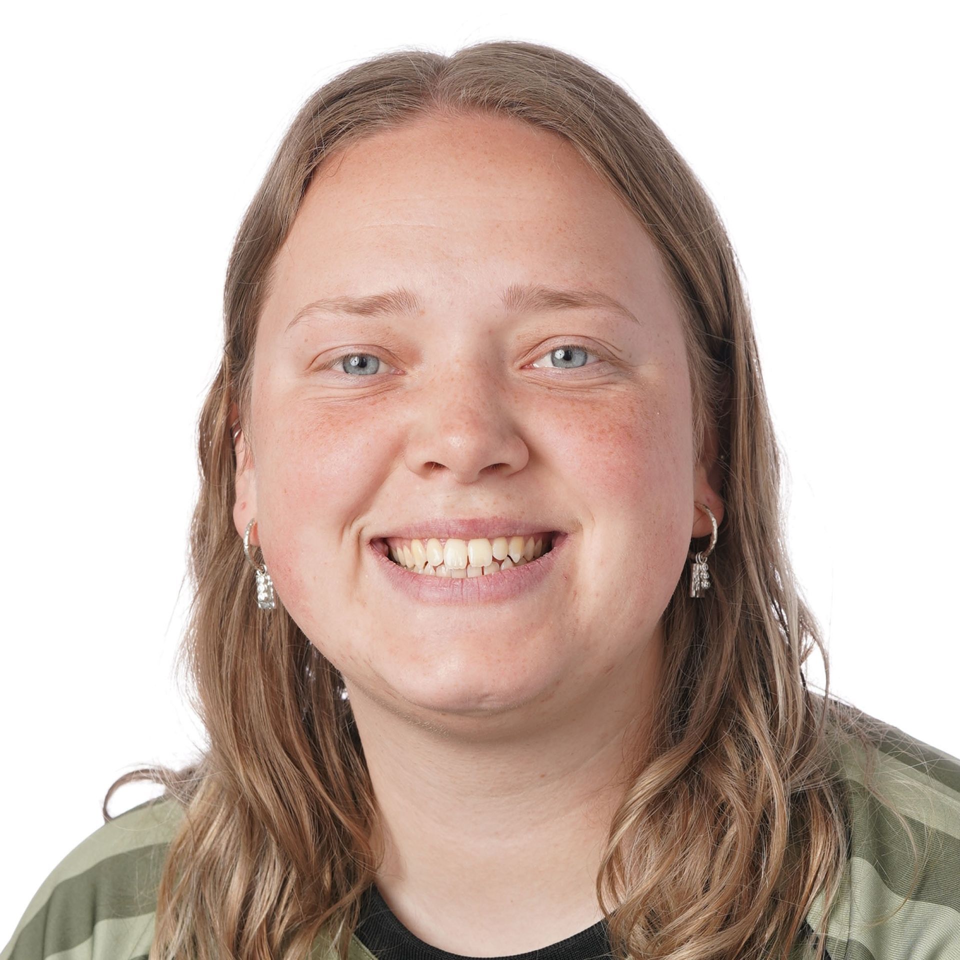 En kvinde med blond hår smiler, iført en lyserød skjorte, foran en stenmur.