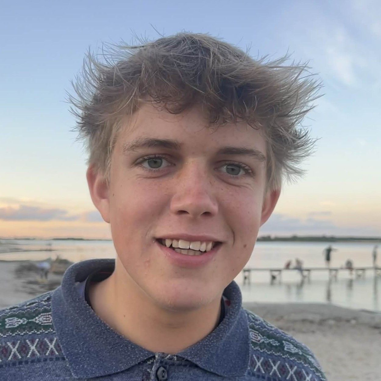 Mand med tyndt hår smiler, iført en orange og hvid skjorte, og ser på beskueren.