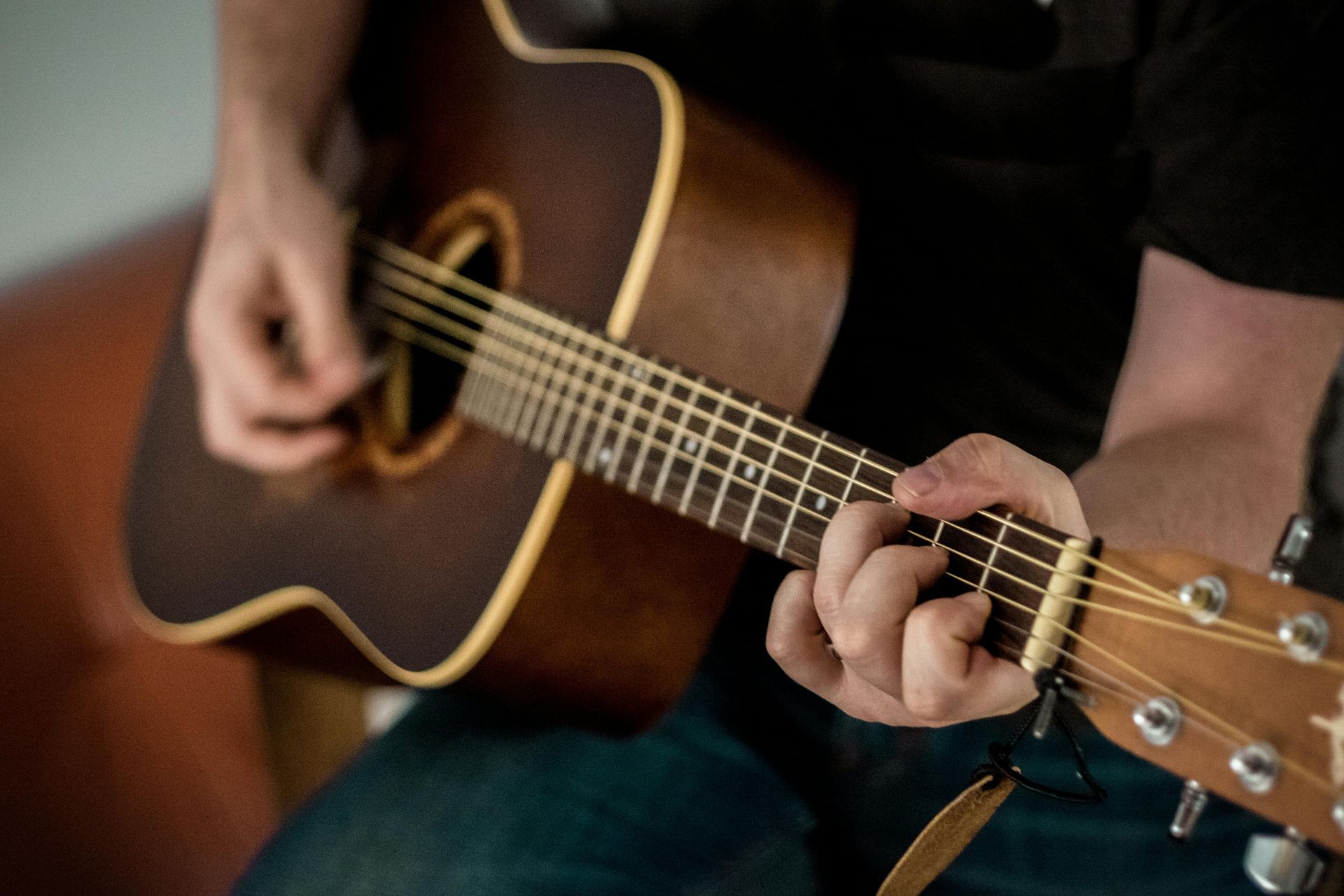 Person spiller på en brun akustisk guitar, fingre på gribebrættet, mens han klimprer.