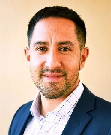 A man in a suit and plaid shirt is smiling for the camera.
