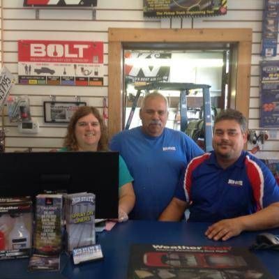 Three people behind a counter in an auto parts store. The employees are smiling.