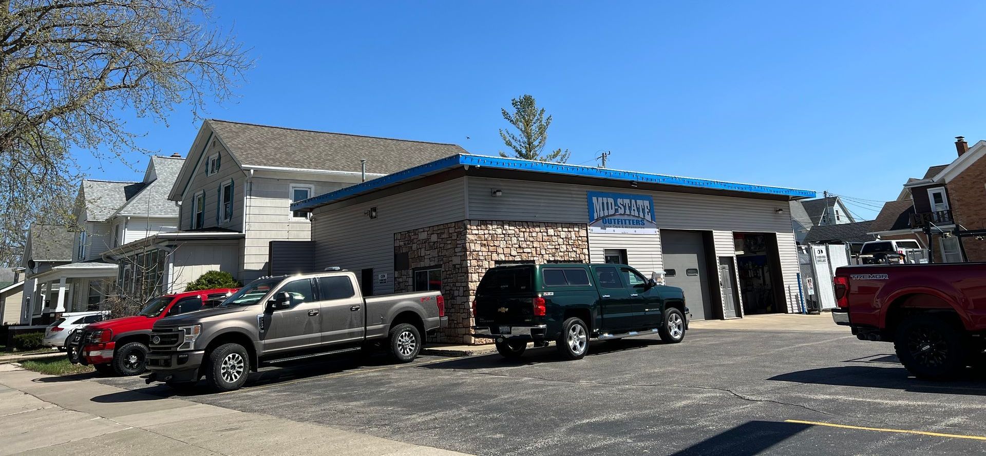 A building with a blue roof and open garage doors, with parked trucks on a gravel lot.