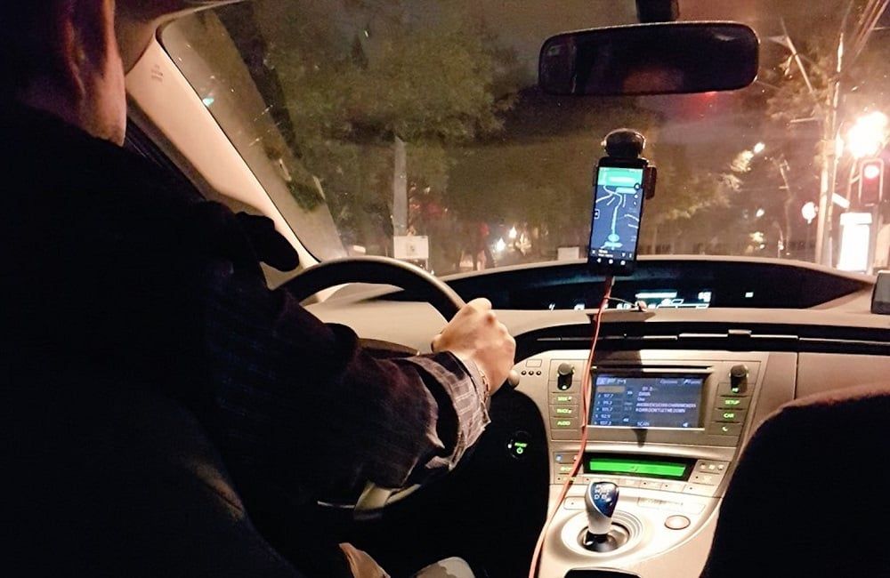 Un hombre conduce un coche con un teléfono en el salpicadero.