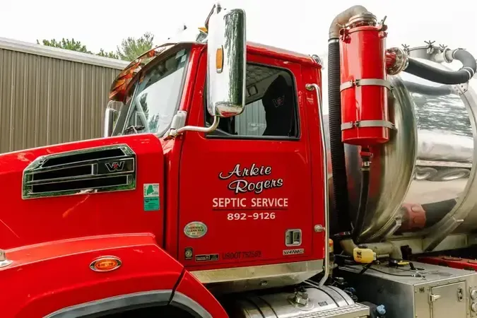 A red Arkie Rogers septic service truck is parked in front of a building