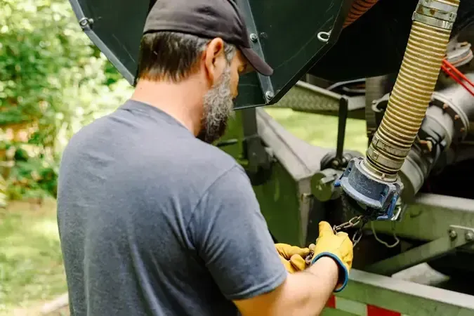 Person in a gray shirt and gloves inspecting machinery outdoors near a trailer