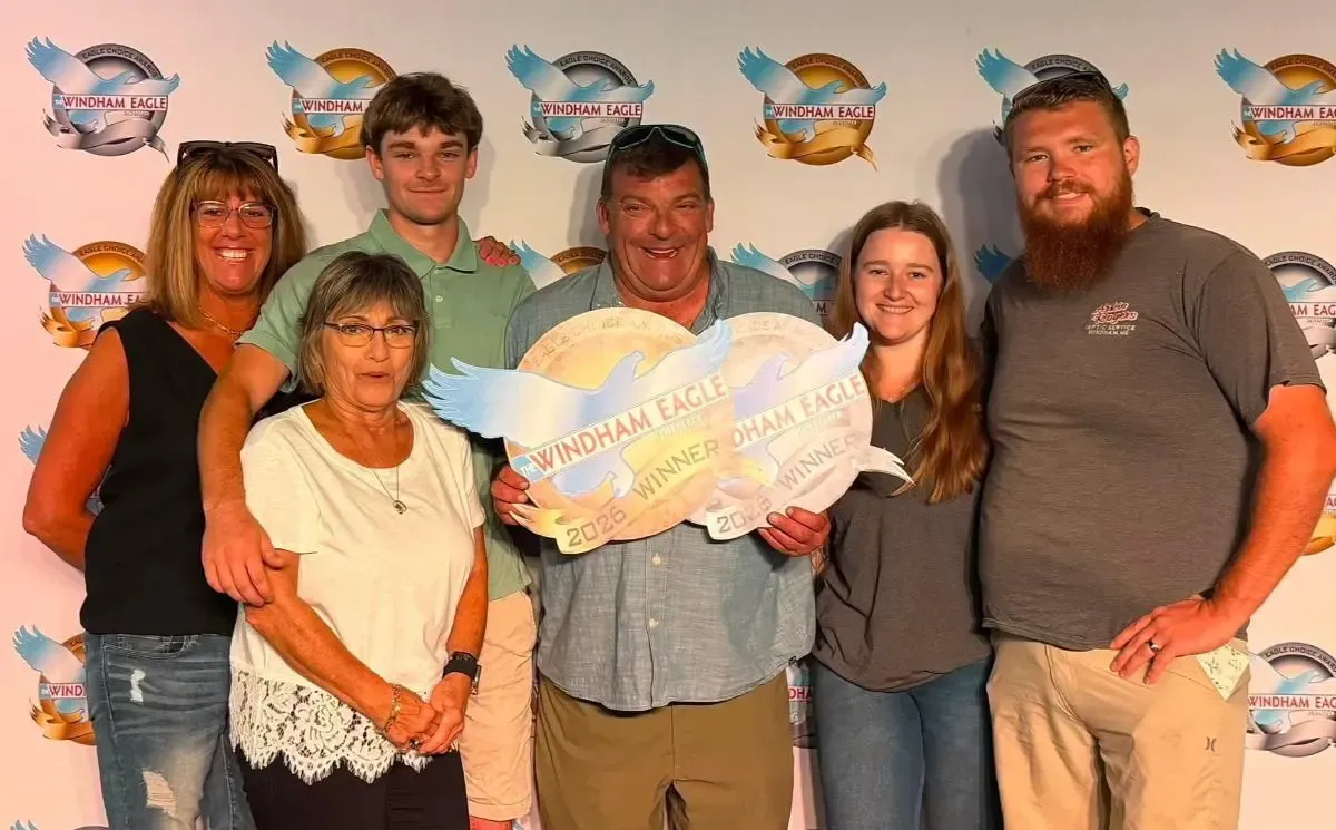 Six people posing with a large colorful sign in front of a logo backdrop at an event