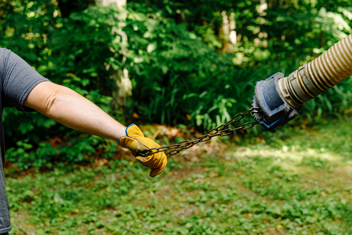 Two gloved hands pull apart a chain near a leaf blower hose in a green yard