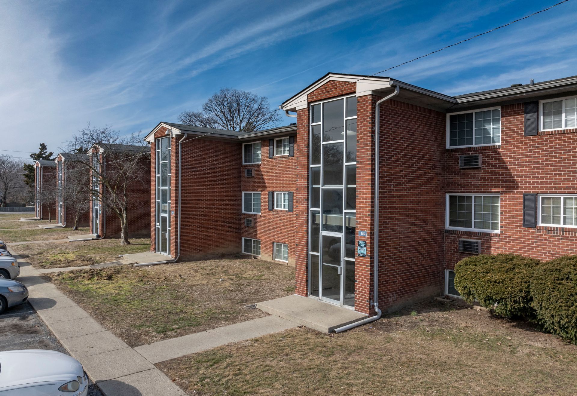 Red brick apartment building on a sunny day. Cars parked nearby, blue sky.