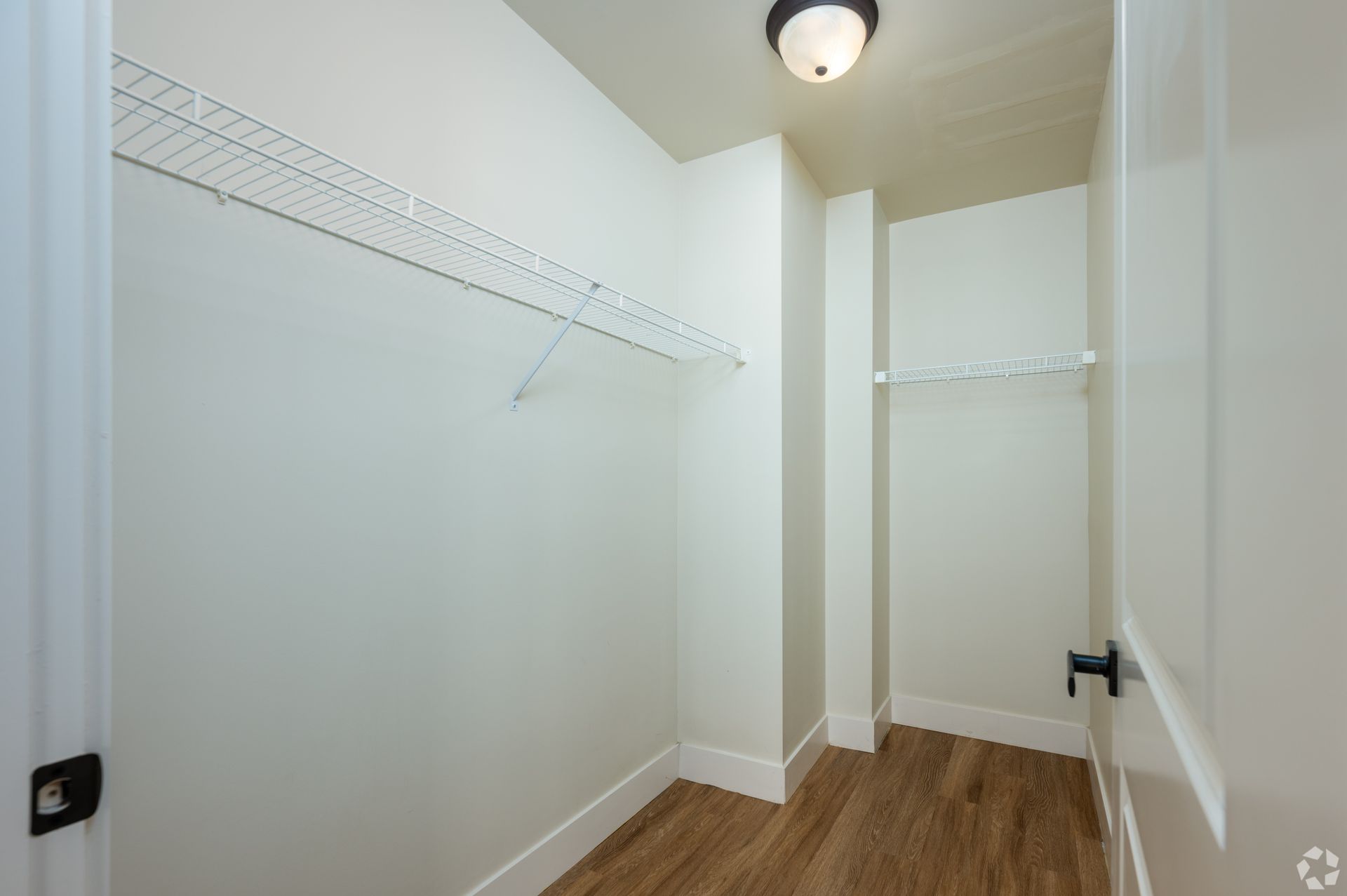 An empty walk in closet with wooden floors and white walls.