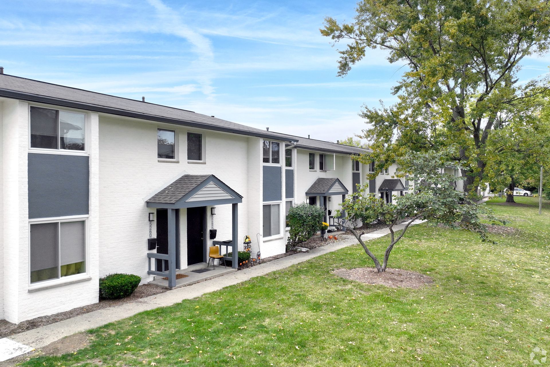 A white apartment building with a porch and a tree in front of it.