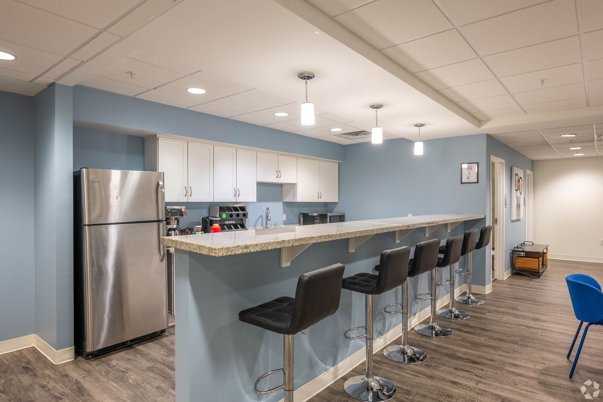 A kitchen with stools , a refrigerator , and a long counter.