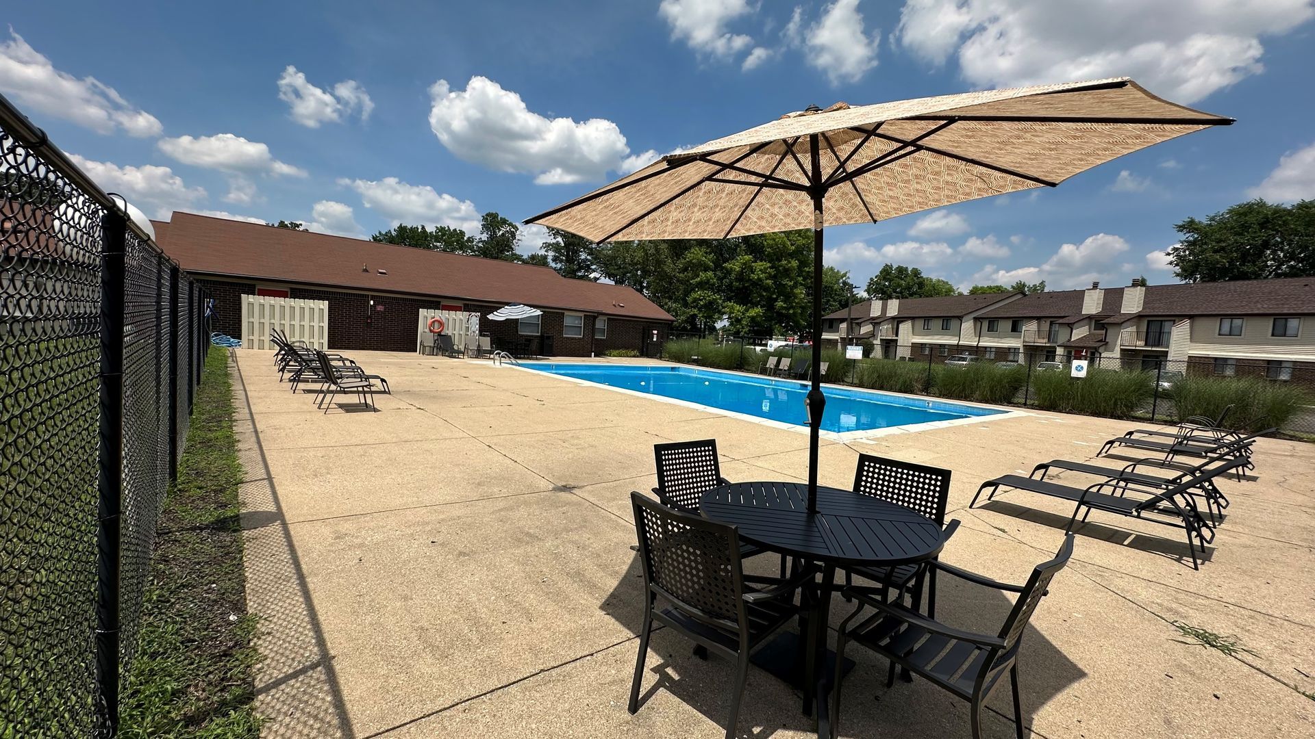 A swimming pool with a table and chairs under an umbrella.