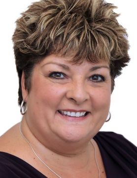 Smiling woman with short highlighted hair wearing a dark top against a white background