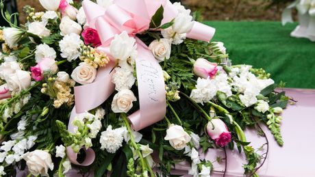A pink coffin decorated with white flowers and a pink bow. A pink coffin decorated with white flowers and a pink bow