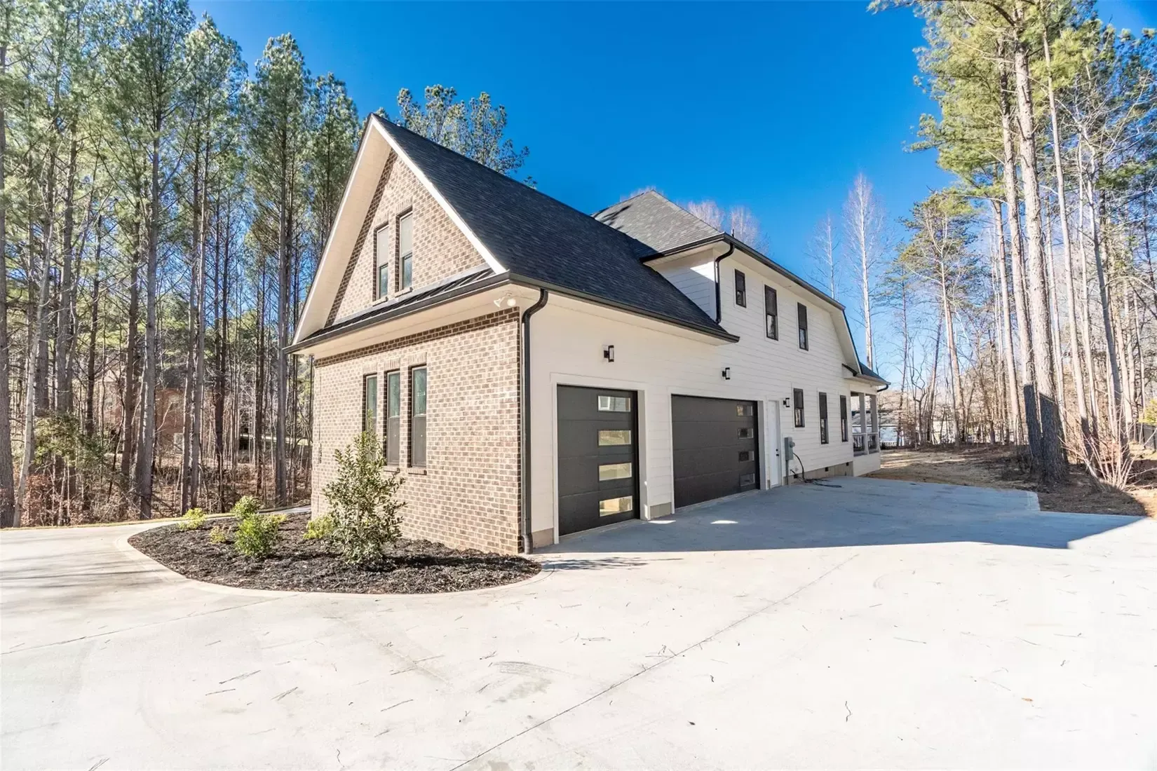 A white house with a black garage door is surrounded by trees