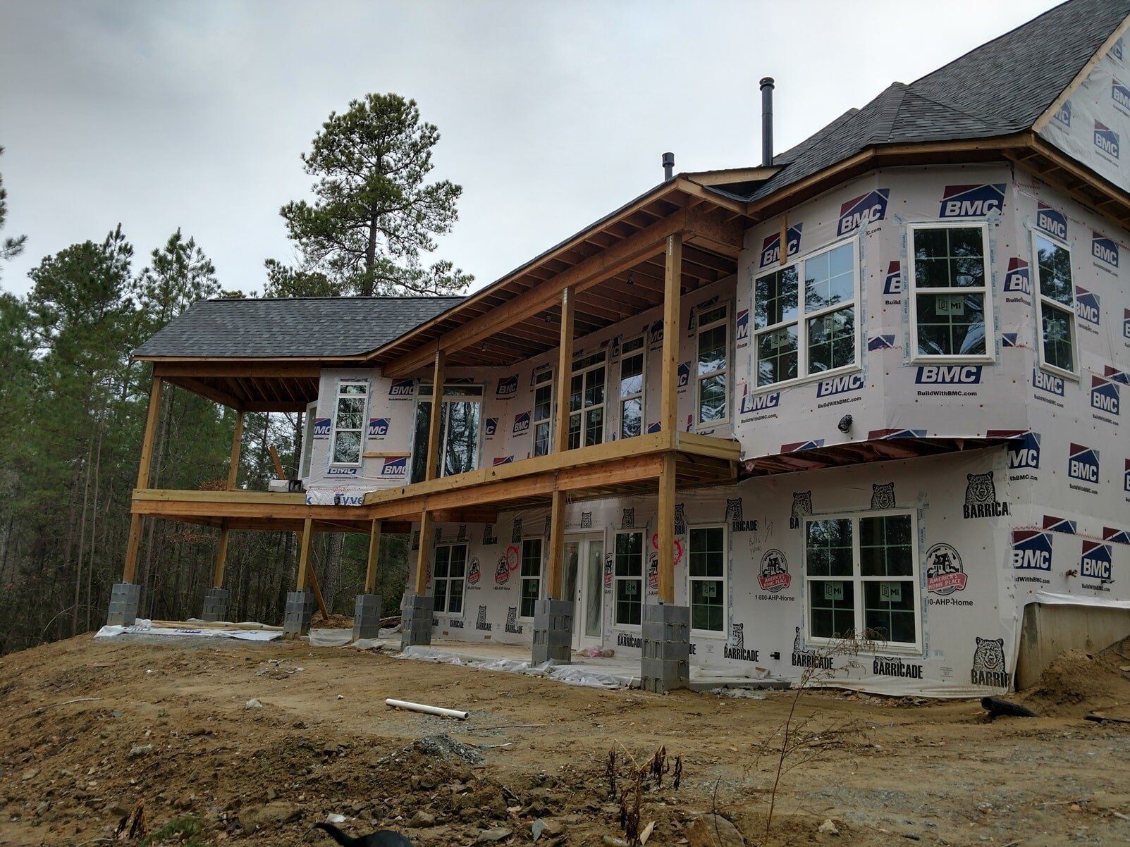 Partially built house wrapped in weatherproofing under cloudy skies, with wooden porch and exposed framing.