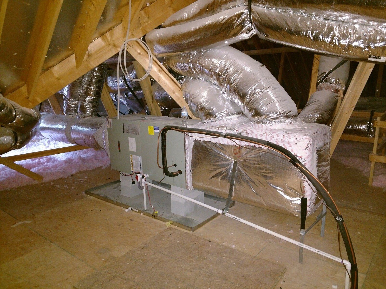 Attic HVAC unit with silver ductwork and wooden roof beams