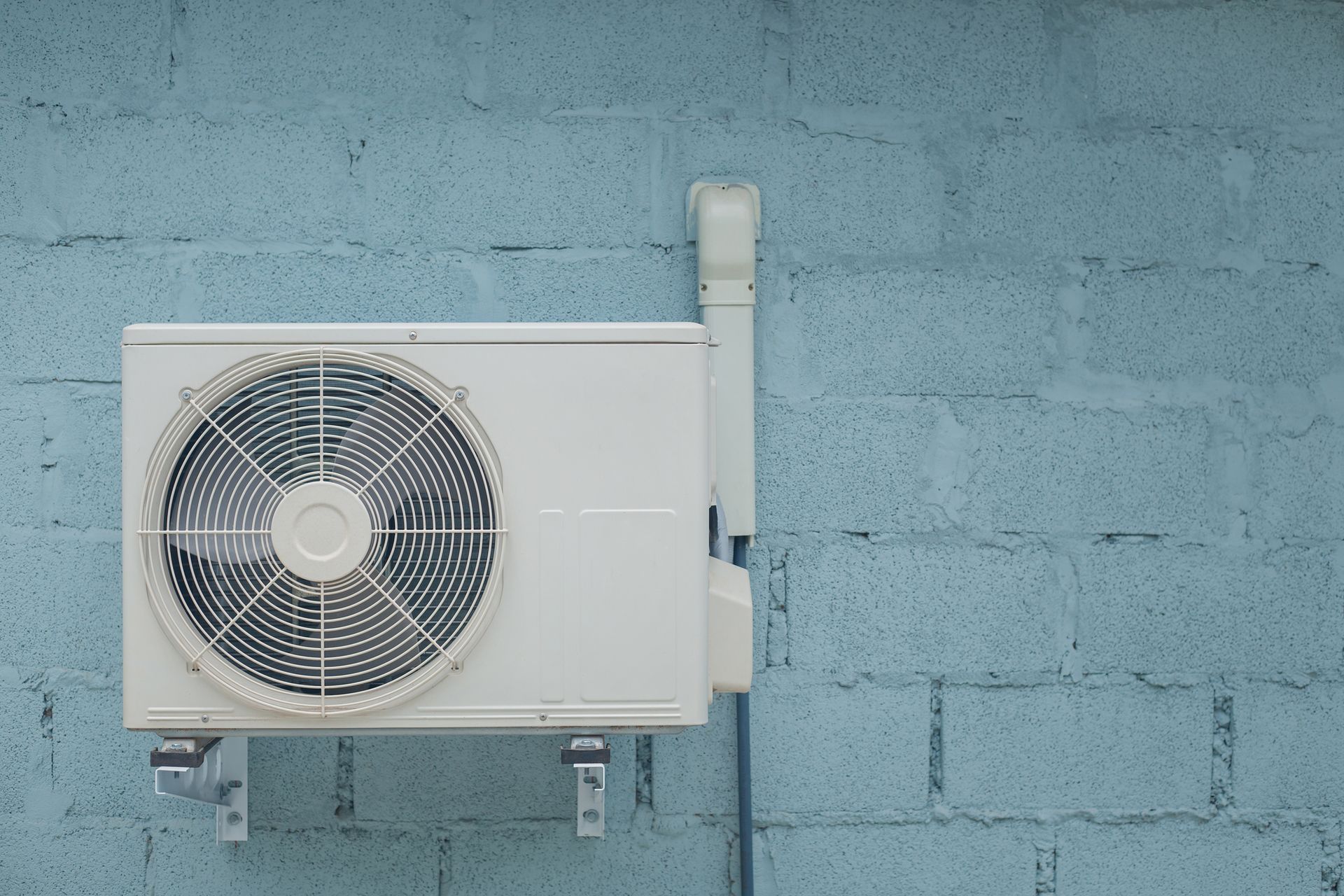 Outdoor air conditioner unit mounted on blue concrete wall for home cooling system. Outdoor air conditioner unit mounted on blue concrete wall for home cooling system.