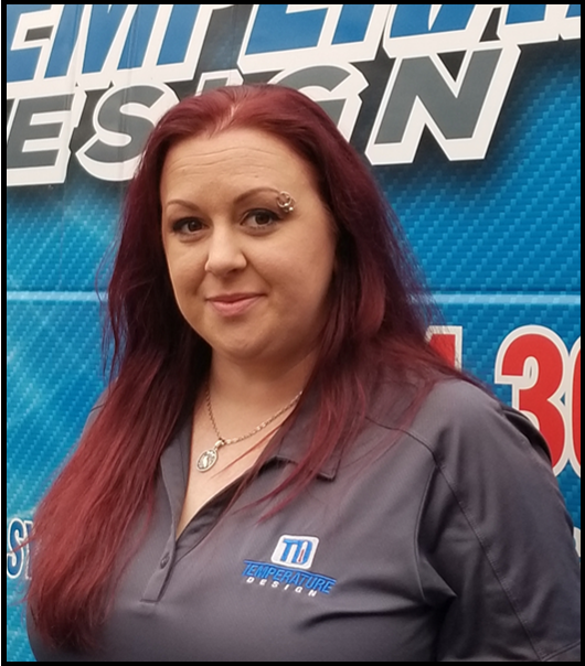 Woman with red hair in a gray polo shirt standing before a blue event backdrop.
