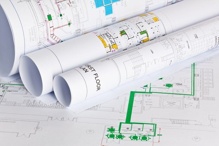 Rolled architectural blueprints with green floor plan markings on a drafting table