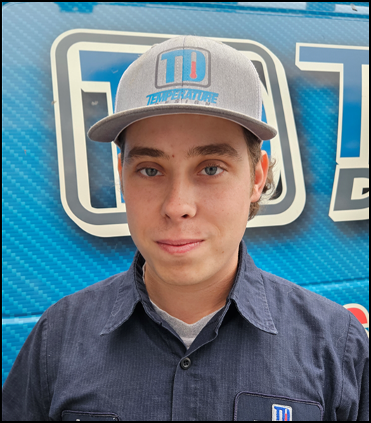 Person in a gray cap and navy shirt standing before a blue branded backdrop.