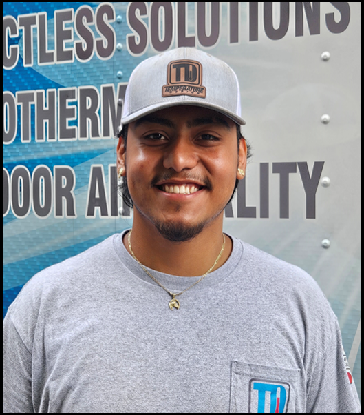 Smiling man in gray T-shirt and cap standing in front of a sign.