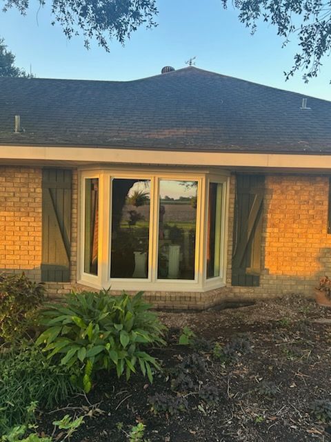Brick house facade with white French doors, green curtains, and a front garden at sunset