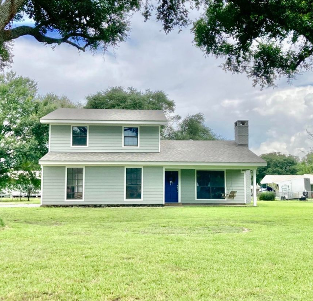 Two-story white house with blue door and large green lawn under cloudy sky