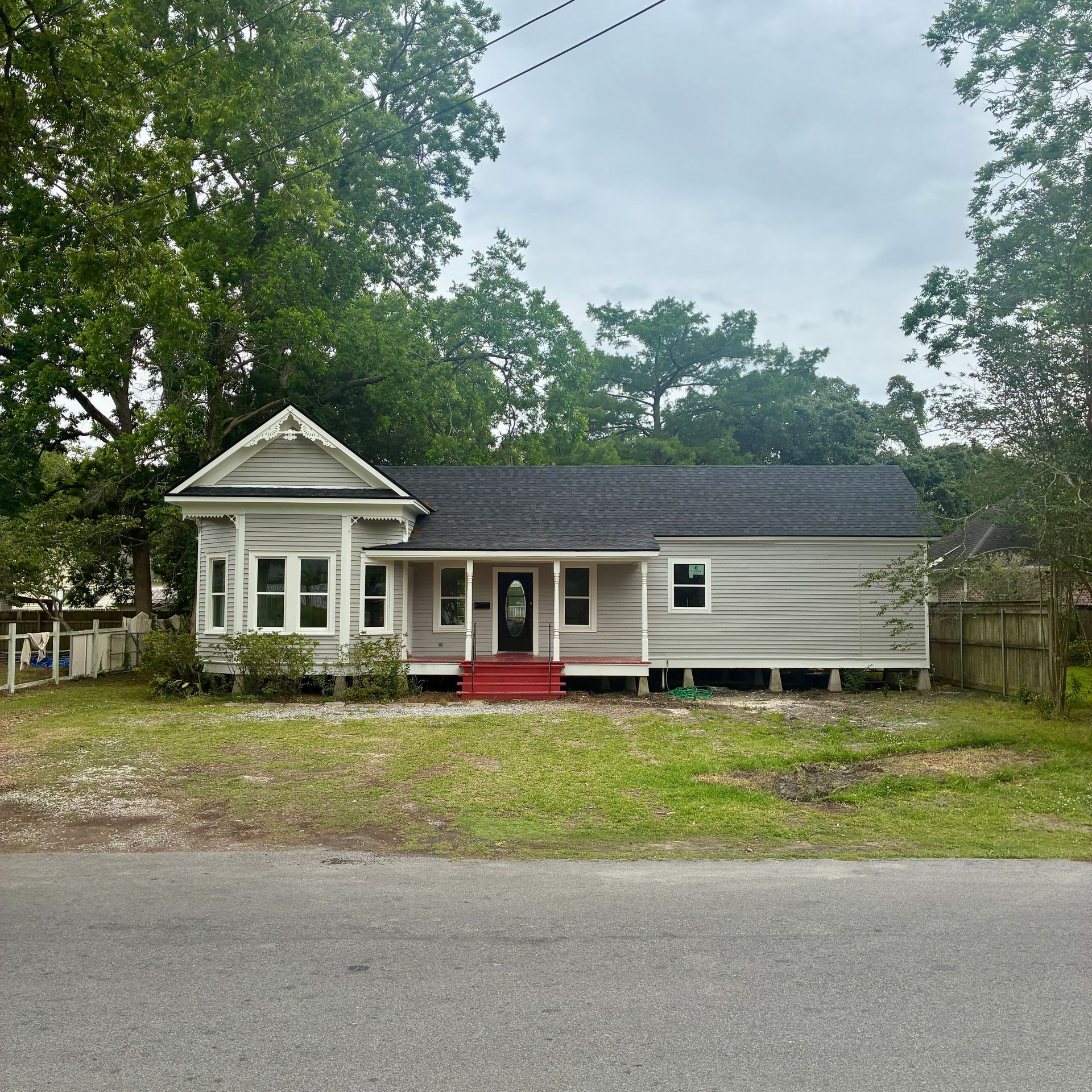 Single-story gray house with red steps on a tree-lined street under an overcast sky