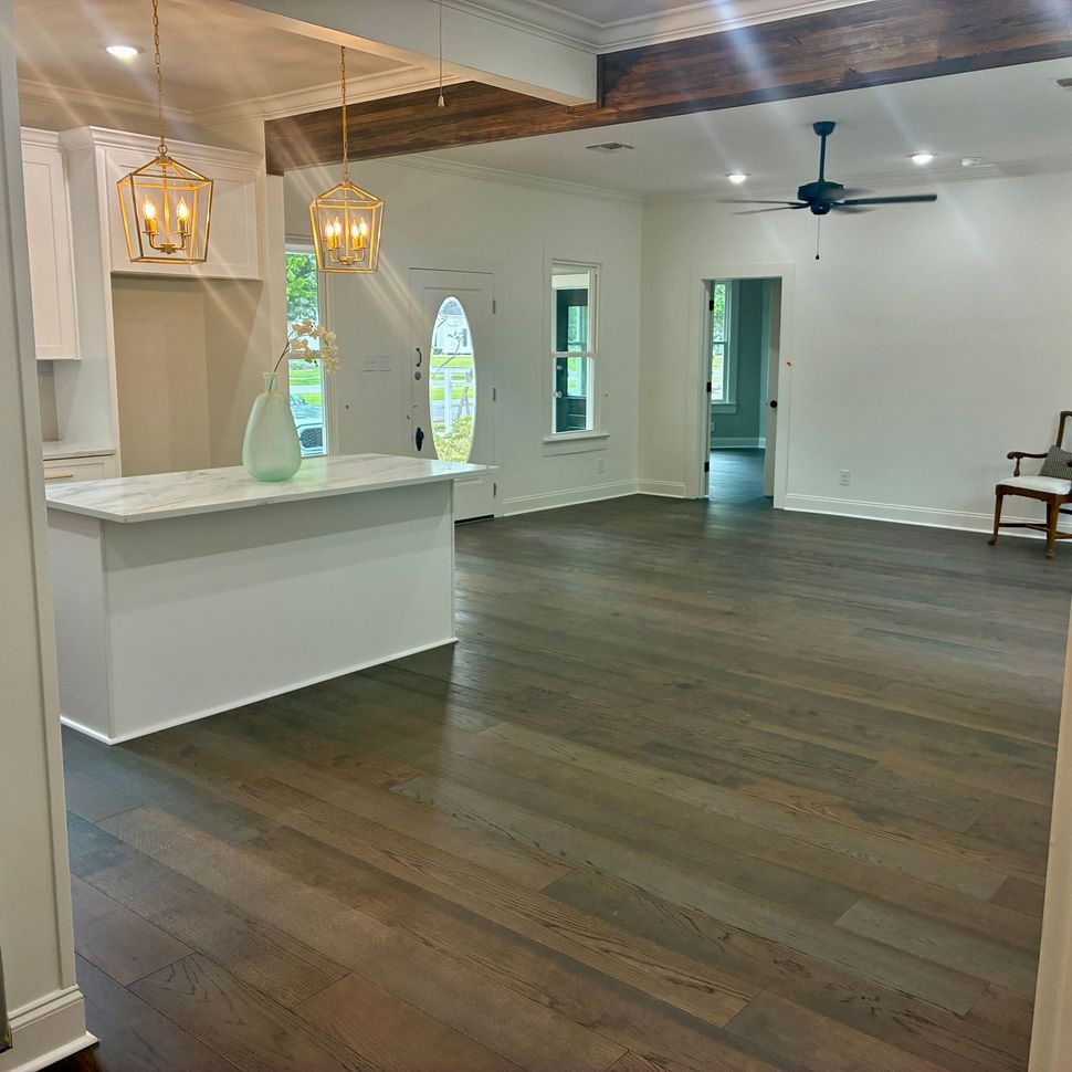 Empty modern living room with dark wood floors, white walls, and hanging pendant lights beside a bar counter
