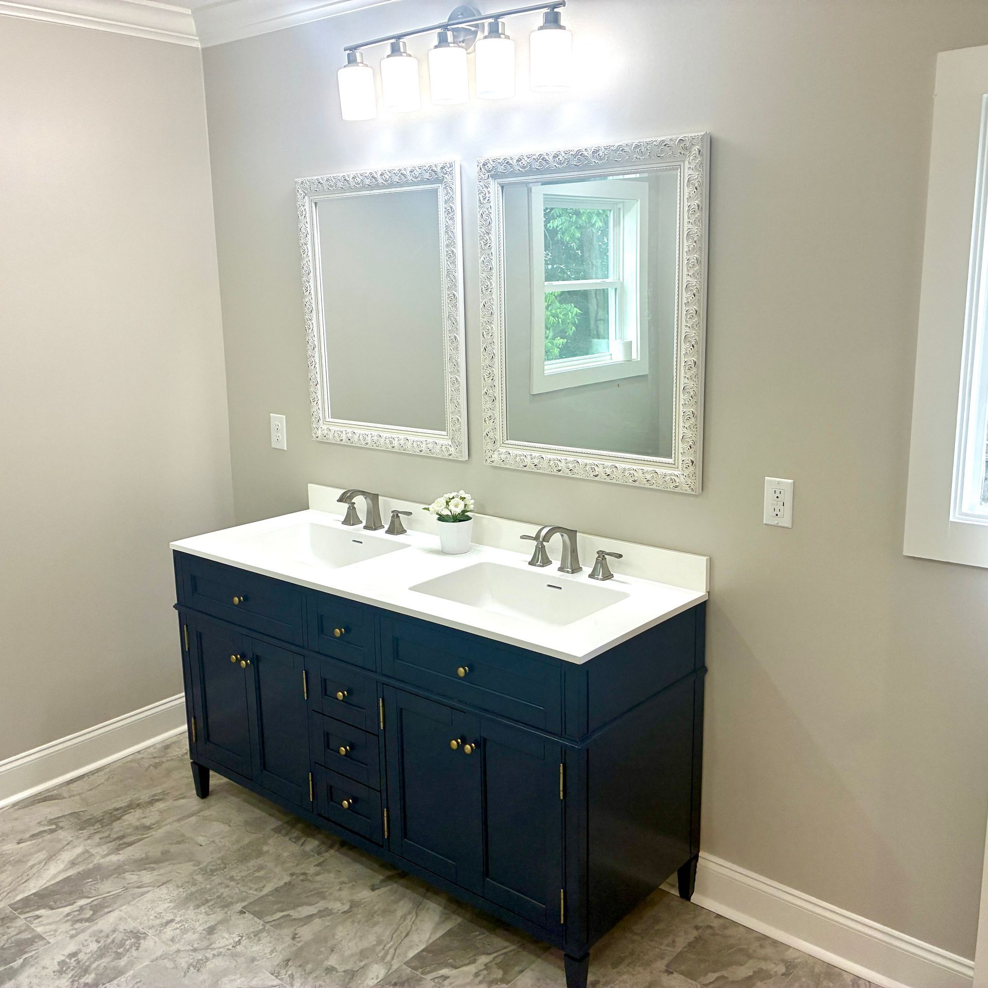 Modern bathroom vanity with navy cabinets, double sinks, and ornate mirrors on a gray wall.