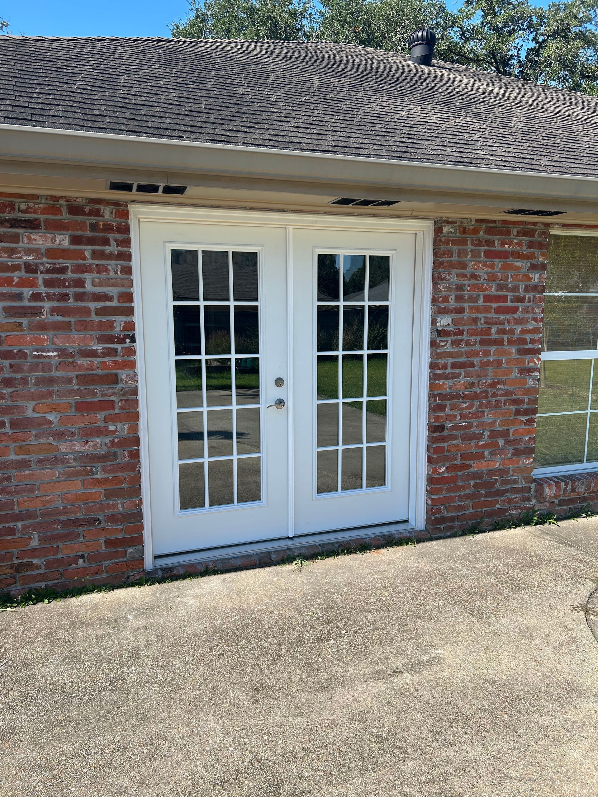 White French doors in a brick building with a shingled roof and paved courtyard.