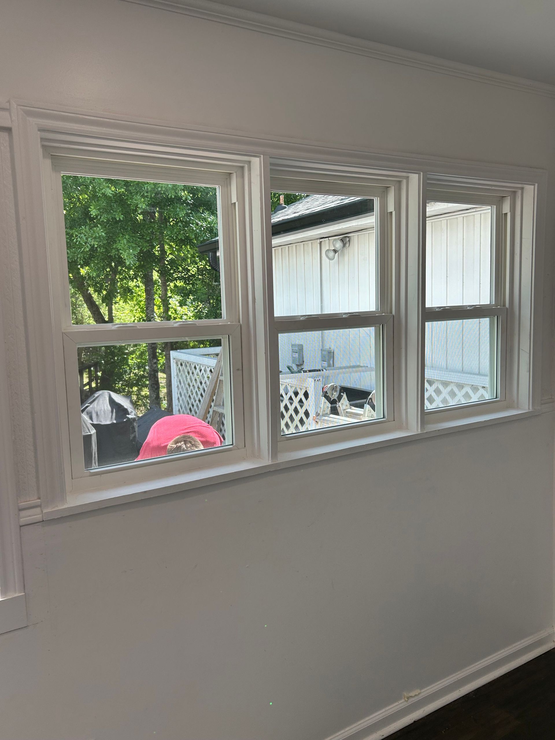 White room with three windows overlooking a backyard with trees and a pink umbrella