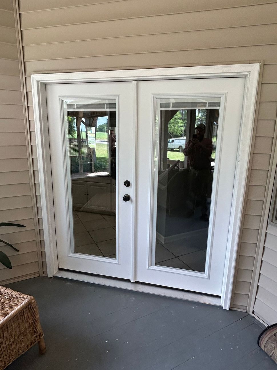 White double French doors on a covered porch with mirrored glass panes and tan siding.