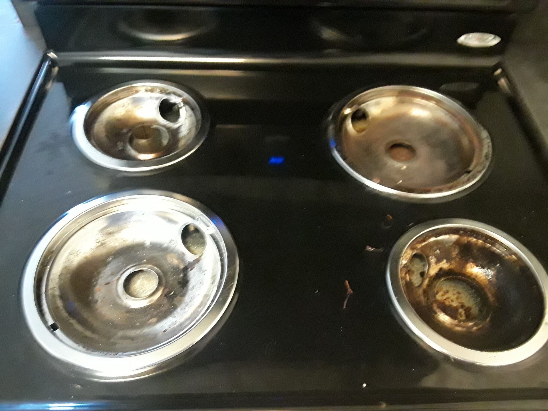 A black stove top with four burners and a blue light
