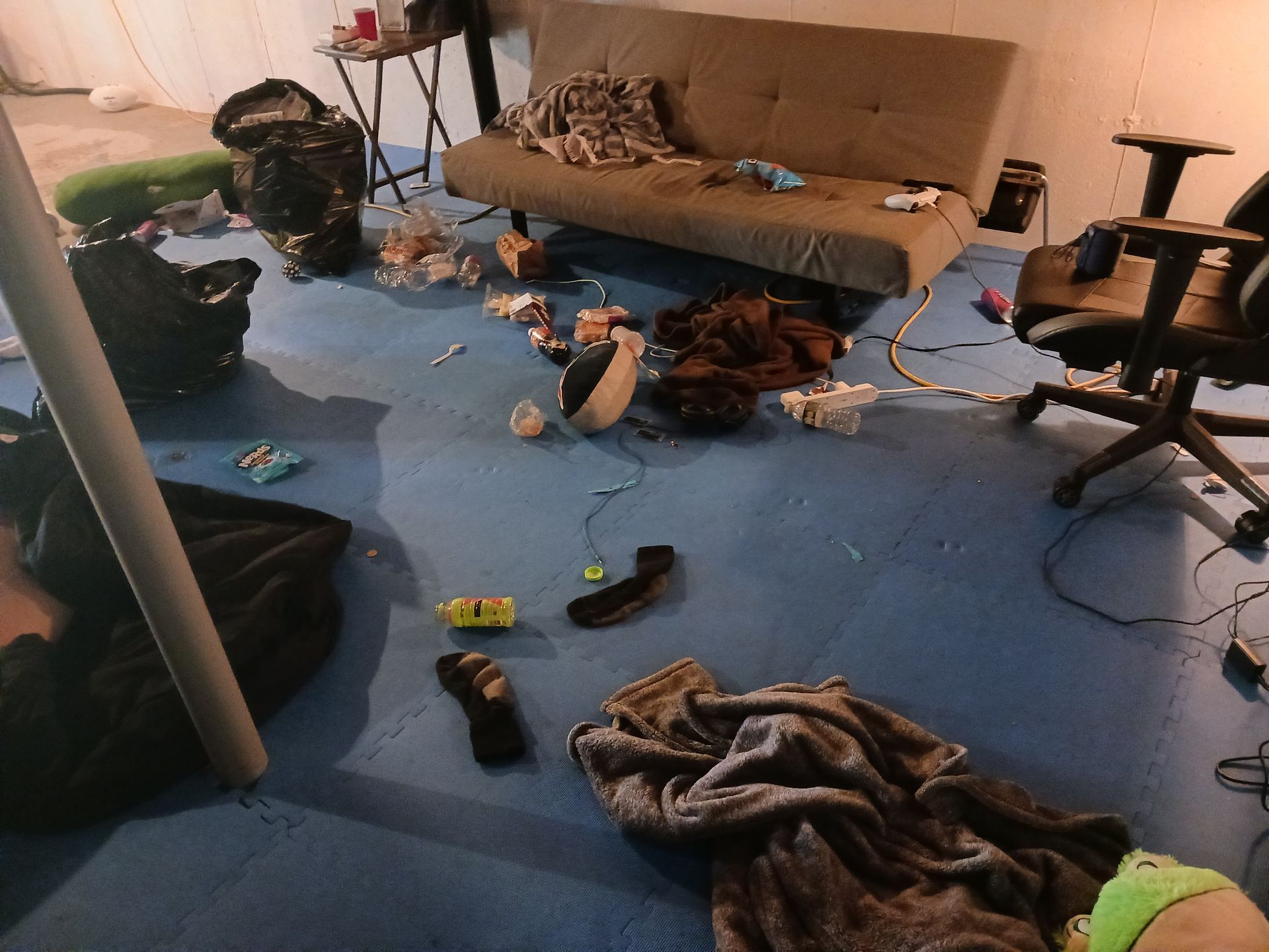 Messy room with a futon, trash, and items scattered on a blue floor.