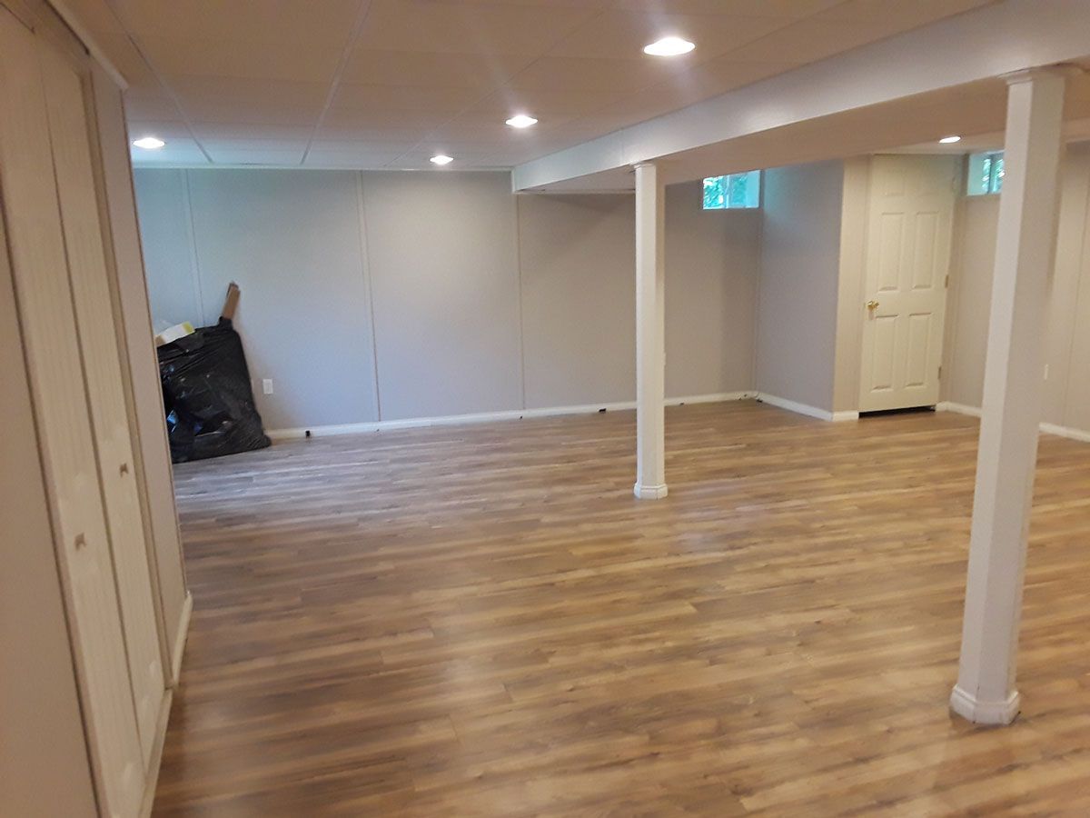 An empty basement with hardwood floors and white pillars.