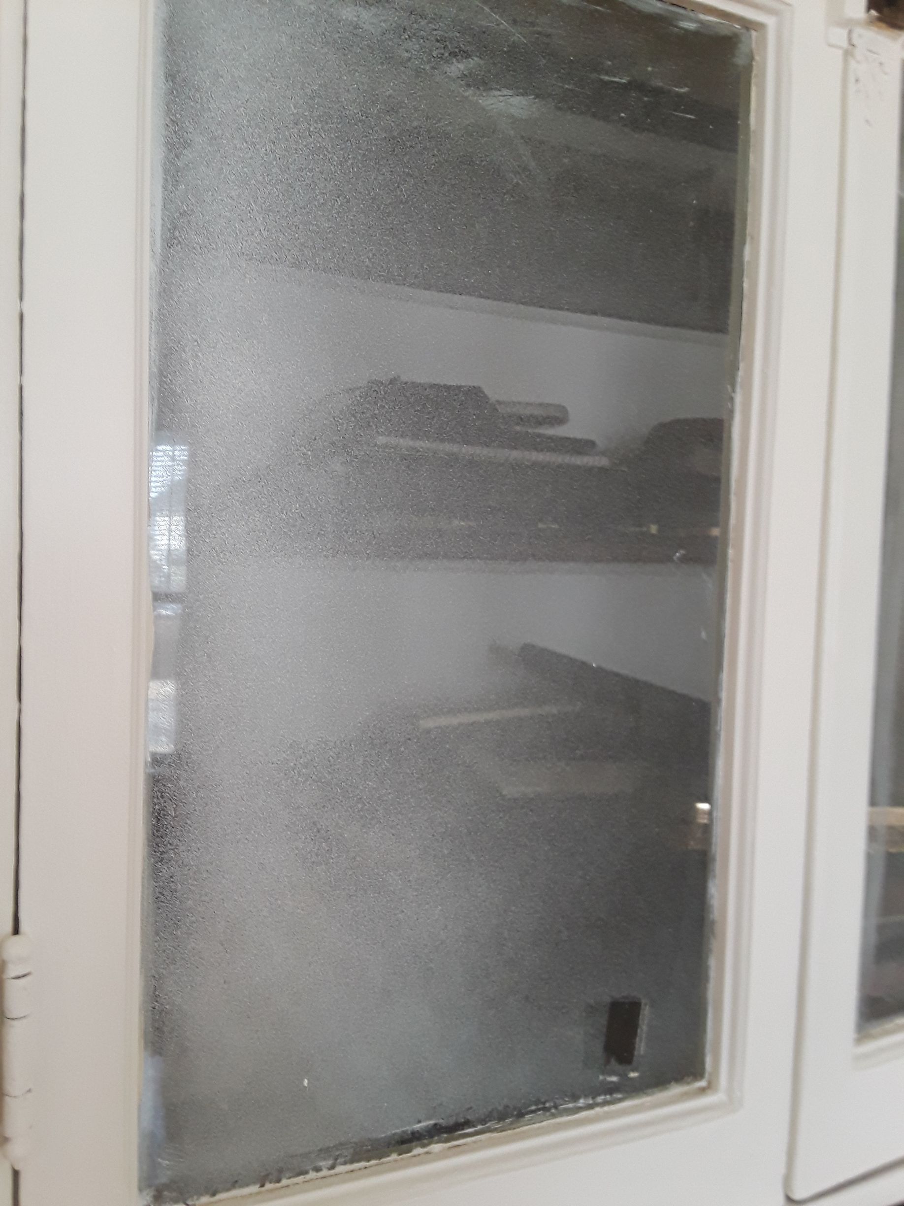 A white-framed glass door with condensation, obscuring view of shelves inside.