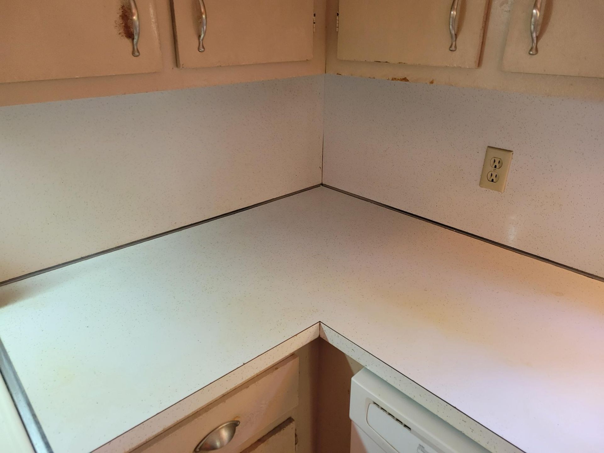 White corner kitchen countertop with cabinets above and below, yellowing with age.