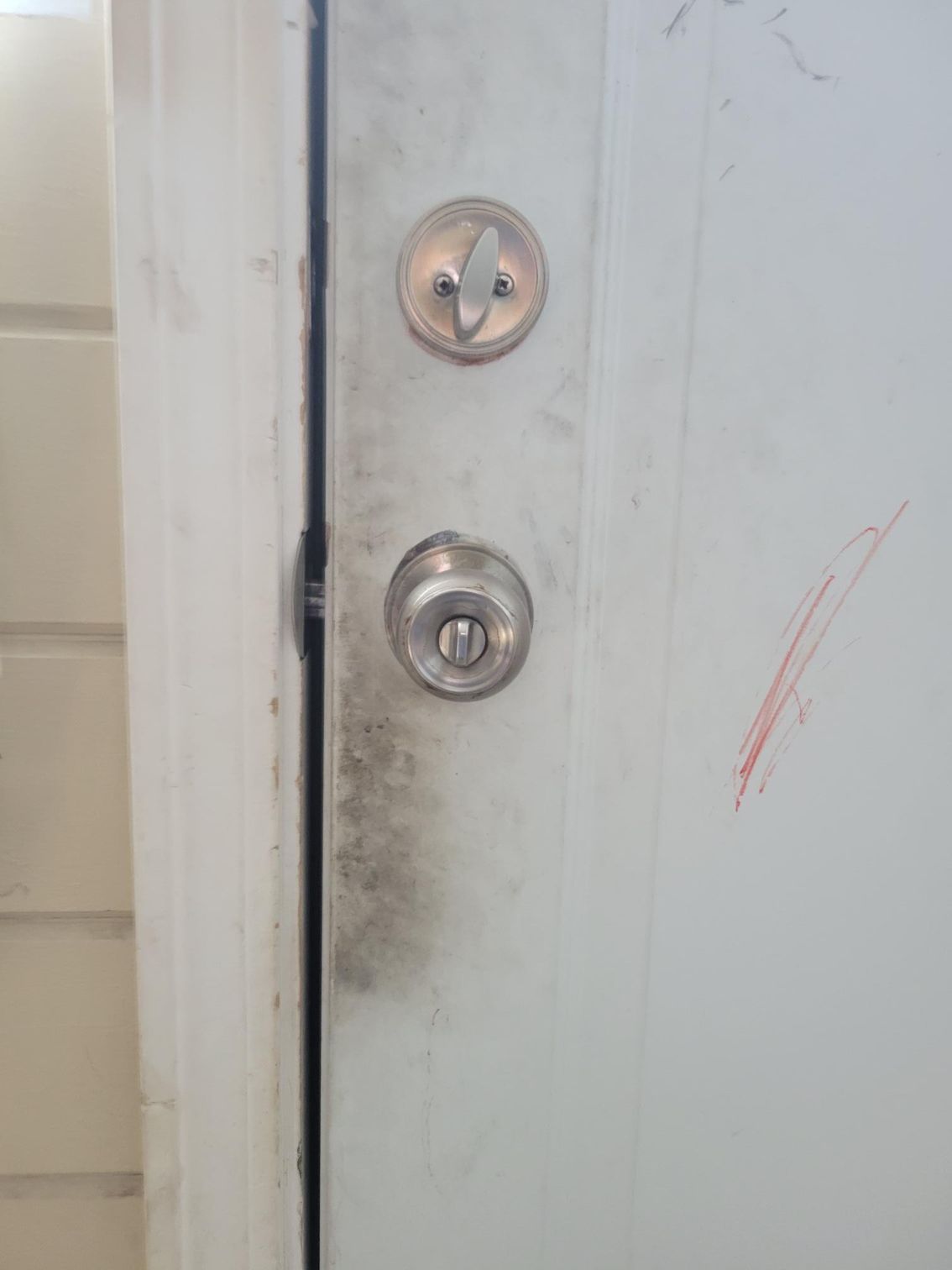 White door with keyhole and doorknob, showing discoloration and a red scratch.