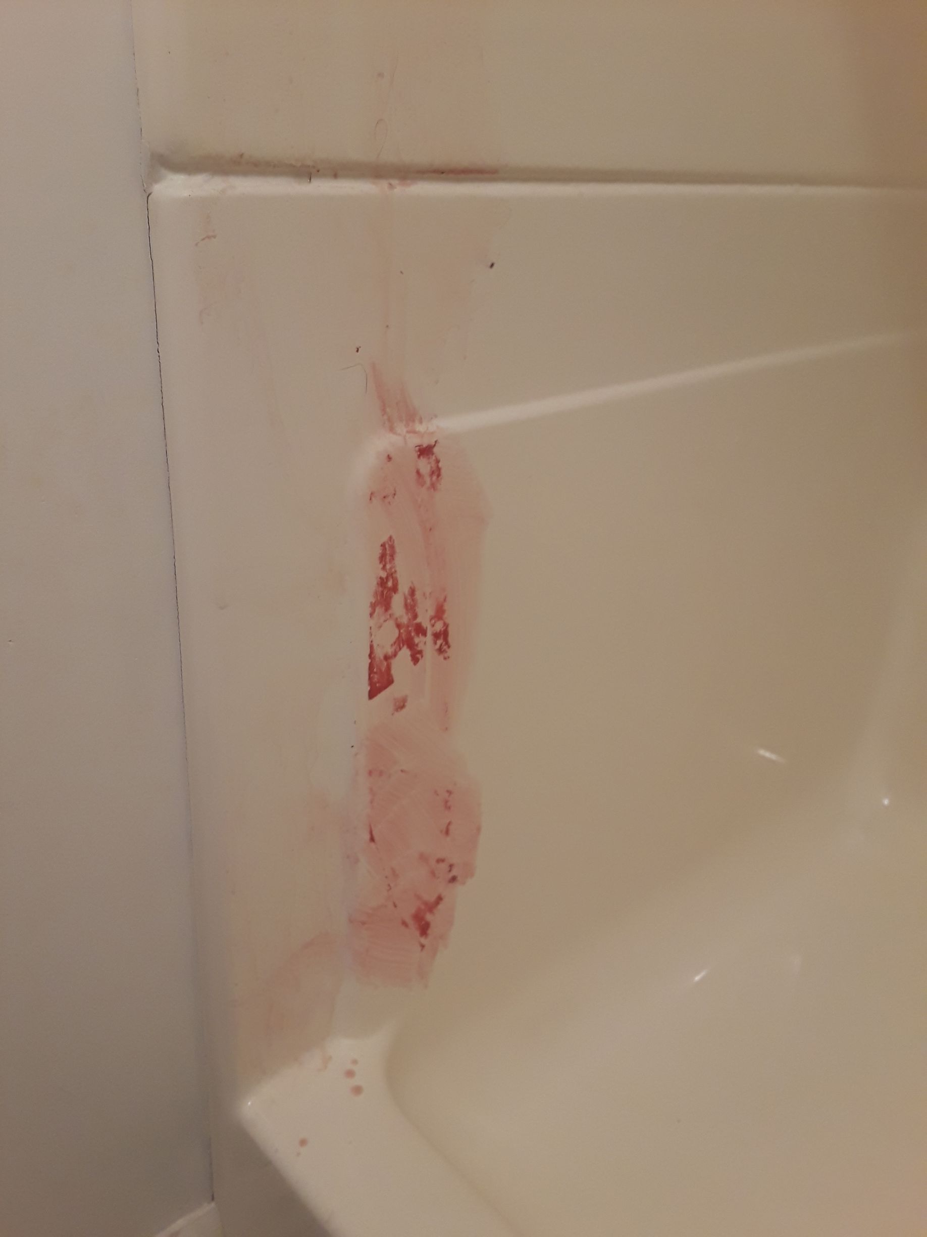 Pink stains on a white bathtub wall, likely from a spill or splash.
