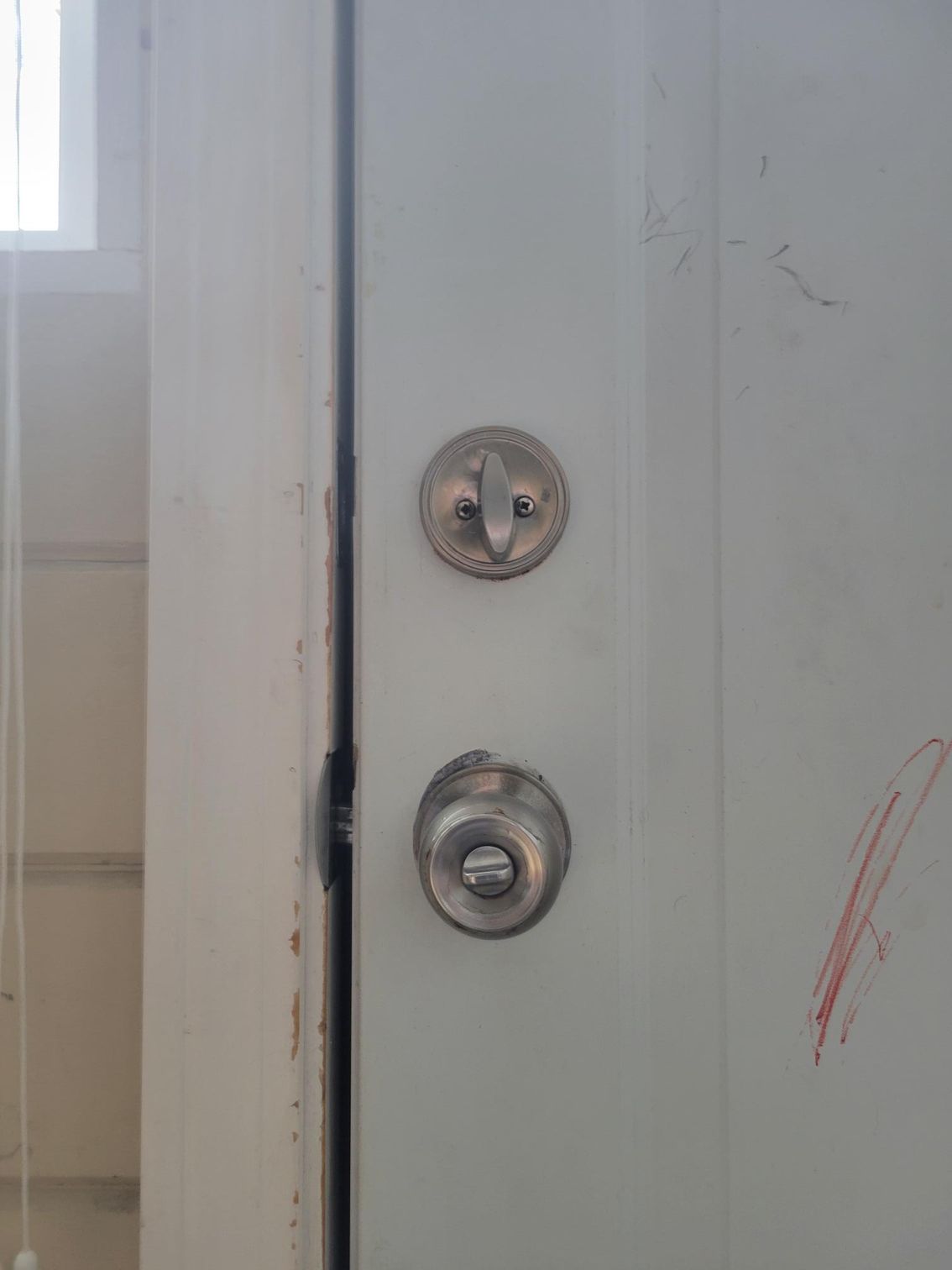 White door with a deadbolt and doorknob. The door has scratches.